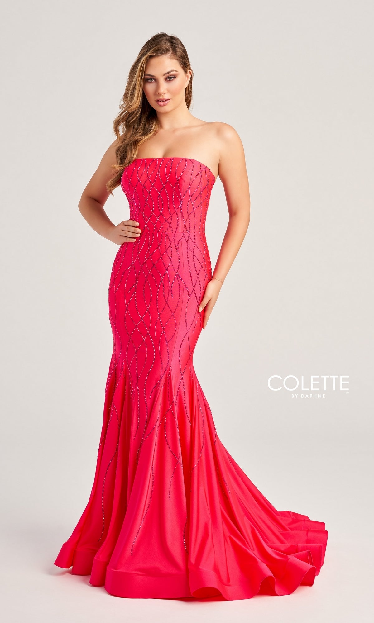 A woman models the Colette Strapless Long Glitter Prom Dress CL5106, a bright pink fitted mermaid gown with subtle sequin and glitter print details. She poses against a plain light background, with